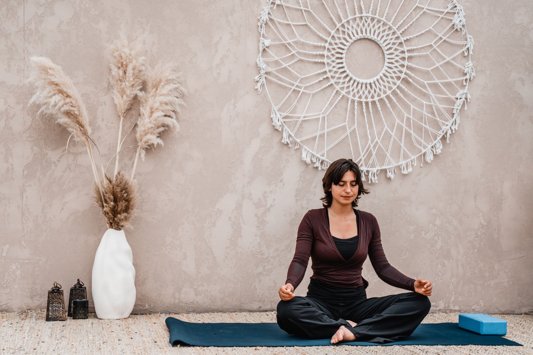 Een rustig zittende yogabeoefenaar bij de lichte wand met macramé